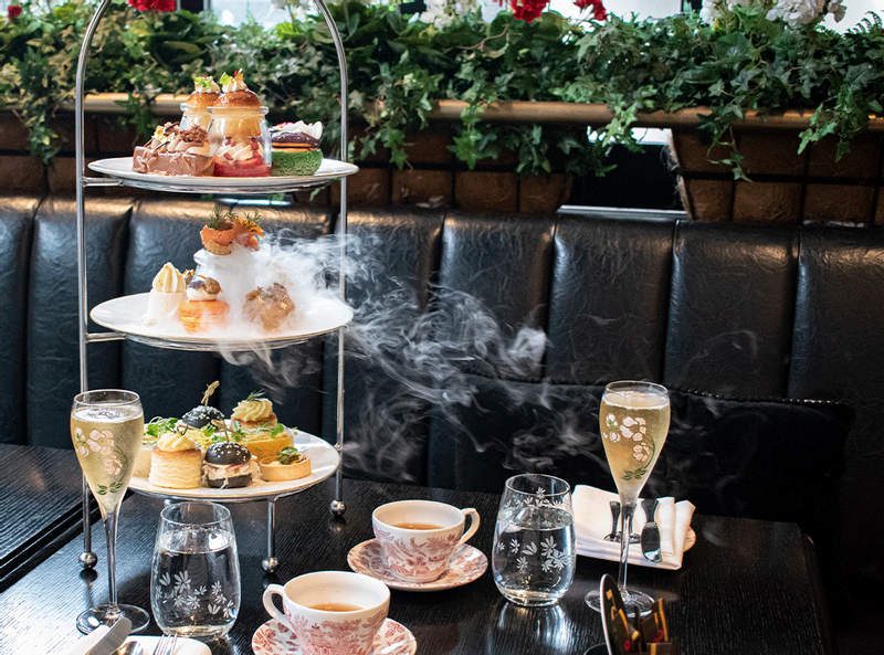 A stand of three tiers containing sweets and savouries with champagne glasses and tea cups