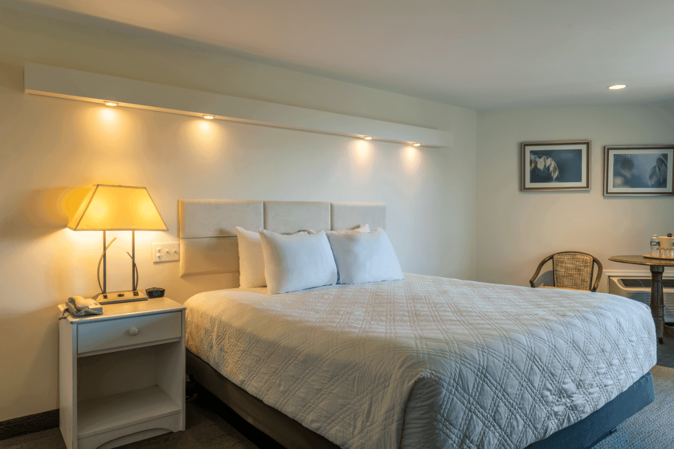 A hotel room with a large bed, nightstand, lamp, chair, and artwork on the walls.