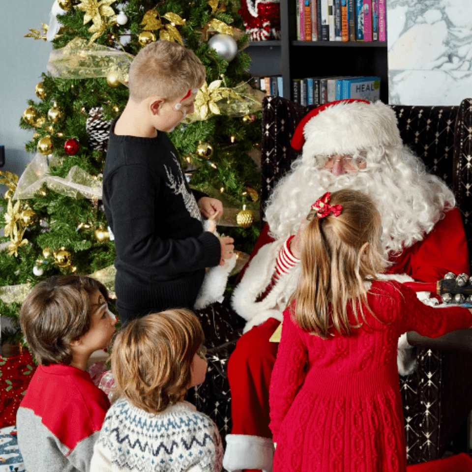 Children visiting Santa by a decorated Christmas tree surrounded by festive ornaments and gifts at Hotel X Toronto
