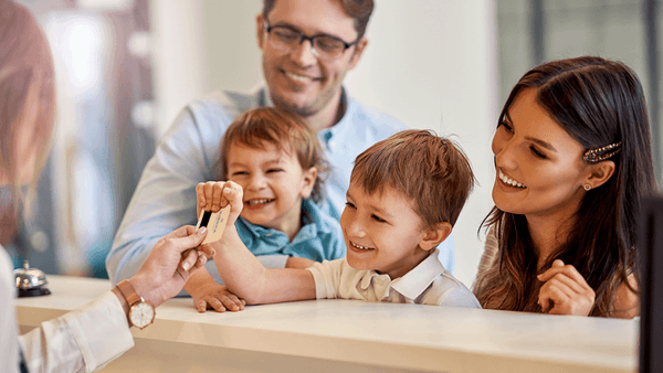 Hotel receptionist greeting a happy family at the front desk at Warwick Hotels and Resorts, giving a key card to the child
