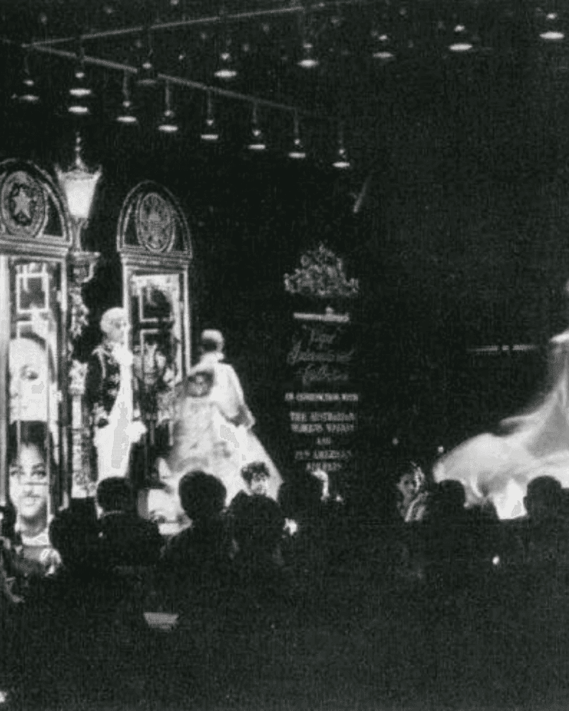 Black and white photo of a stage performance with performers and audience in a theater setting.