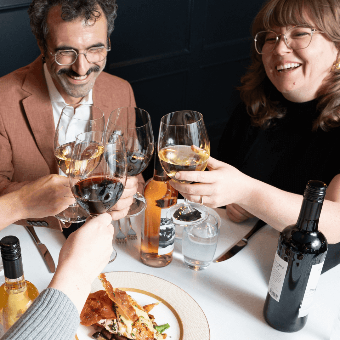 Friends toasting with wine glasses over shared plates during Sunday Funday Happy Hour.