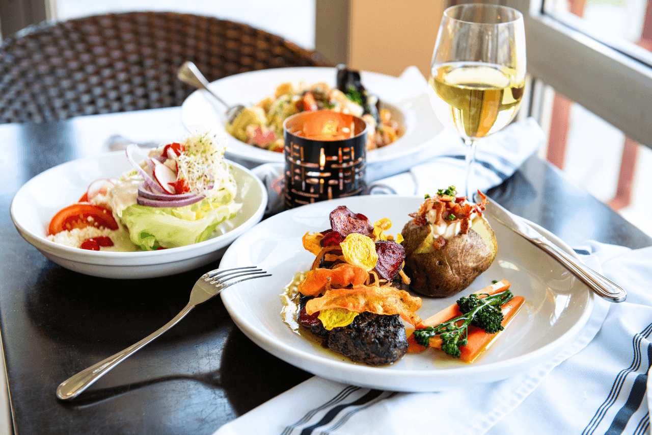A table set with three plates of food and glasses of wine.