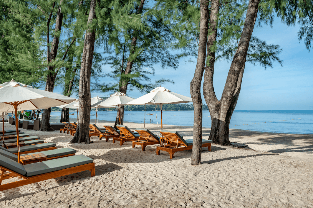 Wooden loungers and umbrellas on a sandy shore facing calm blue waters in NORA Beach Club at Amora Beach Resort Phuket