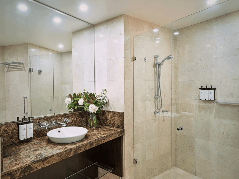 Modern hotel bathroom with marble vanity, large mirror and glass shower enclosure