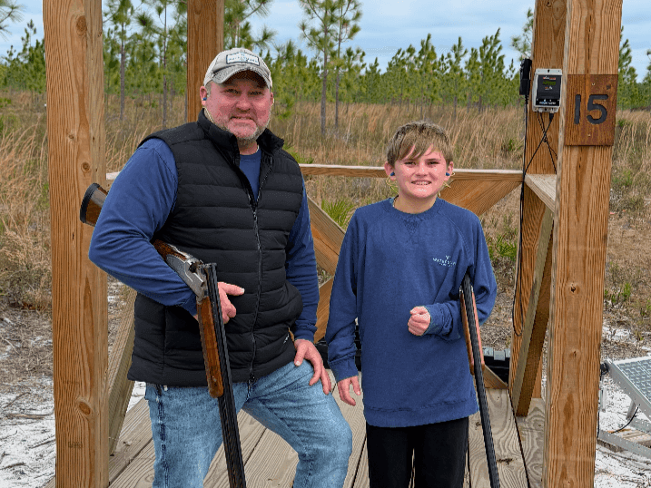 Man and boy with rifles stand on platform with number 15 in woods.