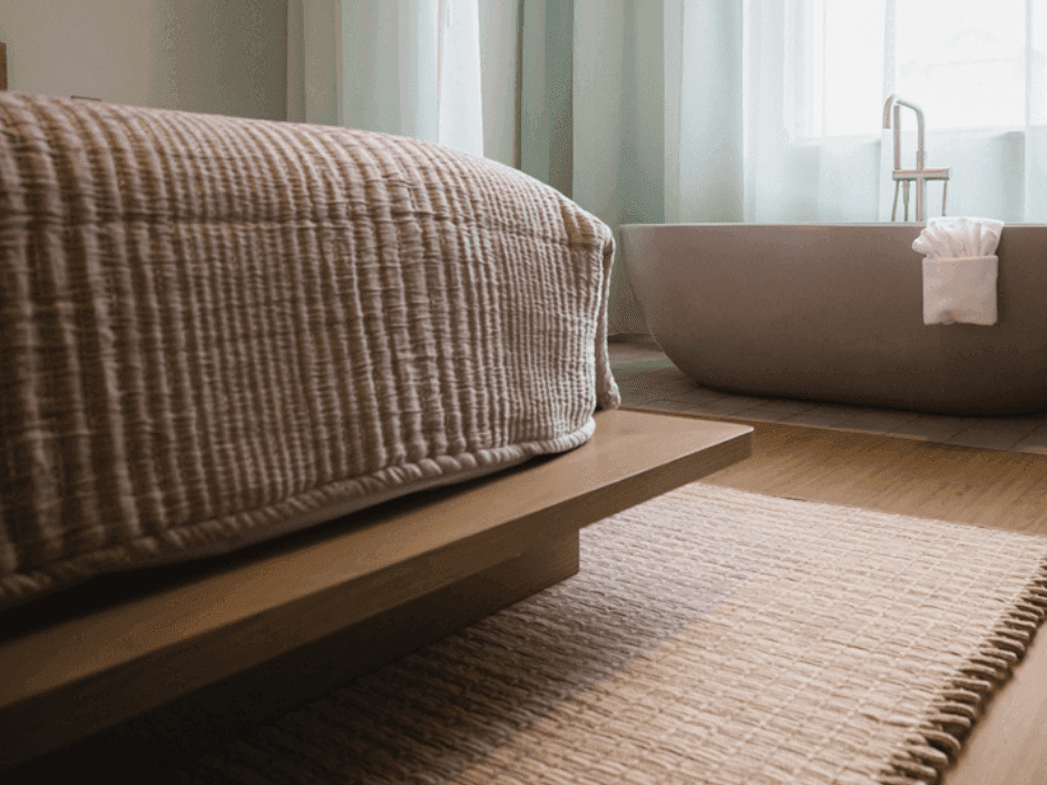 Cozy bed with textured bedding and a woven rug near a bathtub with a white towel.