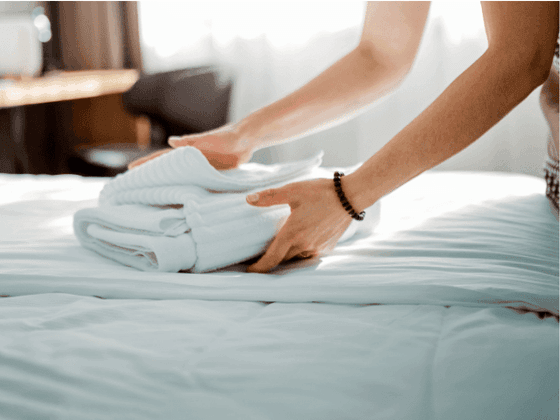 Close-up view of a housekeeper\'s hands neatly folding clean white towels on a freshly made bed at YWCA Fort Canning