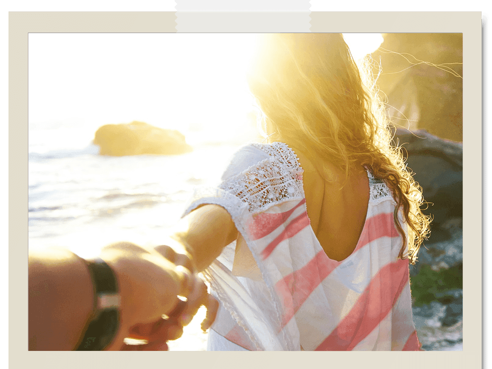 woman on beach in red and white blouse at sunset holding a partner's hand