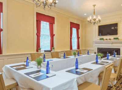 Elegant conference room with a large rectangular table, a fireplace, and red curtains at The Exeter Inn