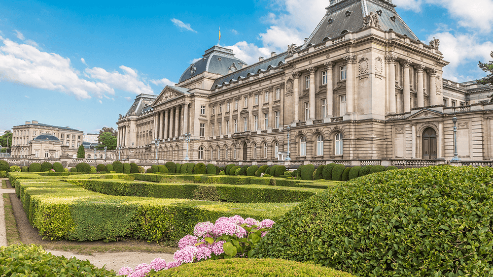 The Royal Palace of Brussels with a beautiful garden under a blue sky.