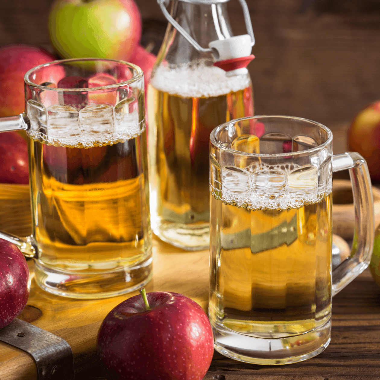 Two glass mugs of golden apple cider beside red apples on a wooden table at Grand Summit Hotel at Attitash