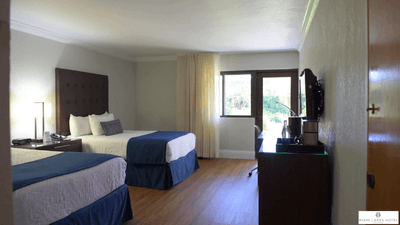 Two beds with tufted headboards near a window overlooking the green garden in the Pool View Deluxe Room at Miami Lakes Hotel