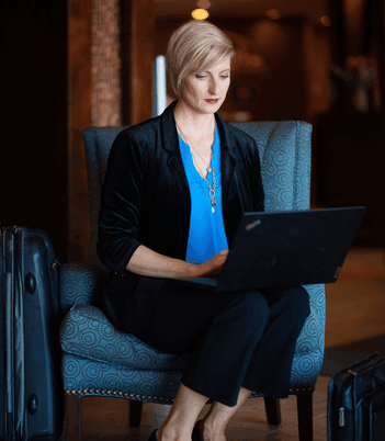 Businesswoman sitting with her luggage and working on a laptop in a hotel lobby armchair at Rodd Royalty