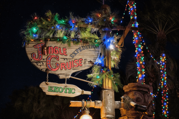 A nighttime shot of a sign reading Jingle Cruise, decorated with pine boughs and Christmas lights at Magic Kingdom. 