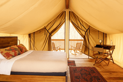 Bed with patterned pillows beside a writing desk inside a safari tent with a balcony at La Tourelle Hotel and Spa