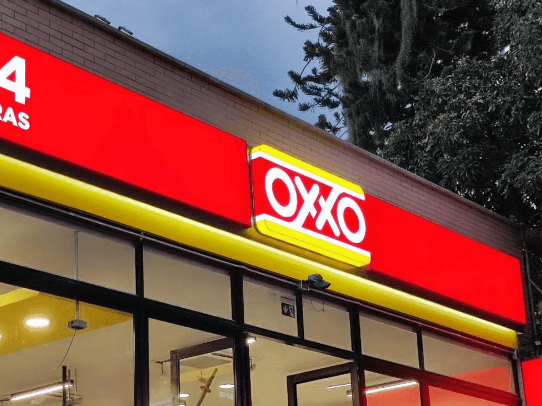 Exterior de una tienda de conveniencia OXXO con su prominente letrero rojo y amarillo, indicando servicio las 24 horas