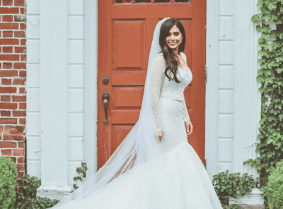 Bride in white gown and veil smiling and posing in front of red door at The Exeter Inn