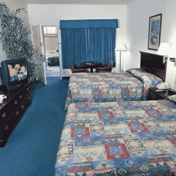 Two beds with patterned bedding in a room with blue carpet and curtains at Grand Legacy at The Park Anaheim.