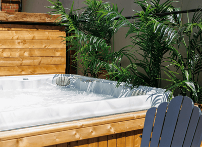 Outdoor hot tub with bubbling water next to potted palms and a blue chair on a sunny wooden deck patio at Rodd Moncton