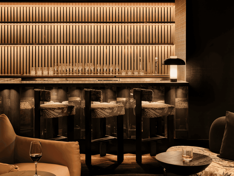 Bar area with three chairs, a lamp, and glasses on shelves in a dimly lit room.