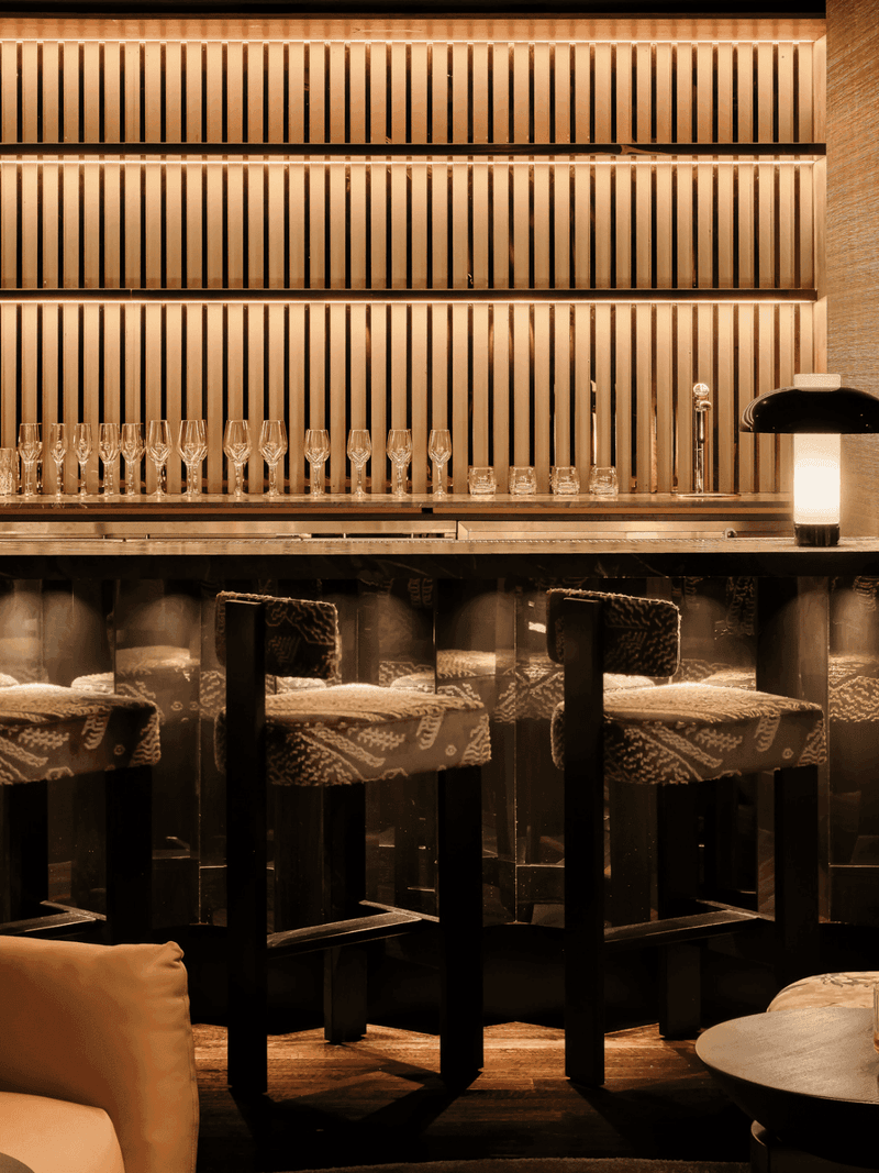 Elegant bar counter with modern shelving, stylish bar stools, and warm lighting, creating a sophisticated drinking atmosphere.