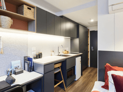 A compact studio apartment with a small kitchen, dining area, and a bed with red pillows.