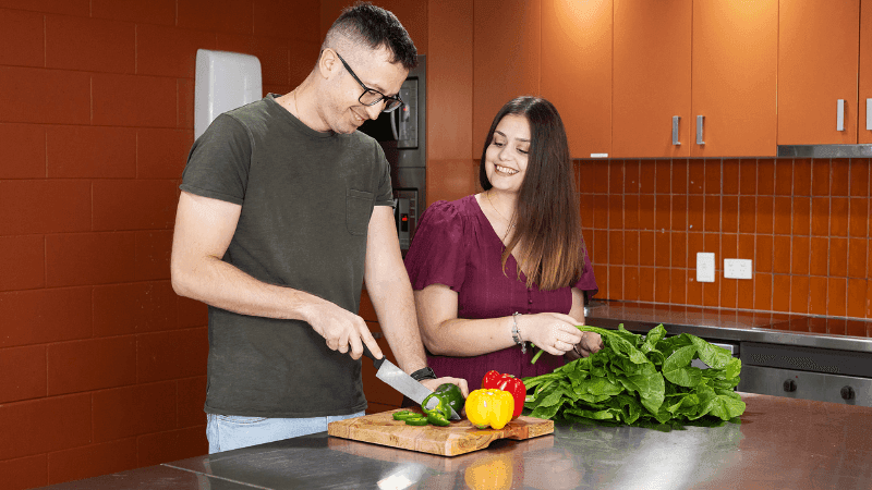 Couple preparing food in the kitchen with vegetables at StudentLiving Darwin.