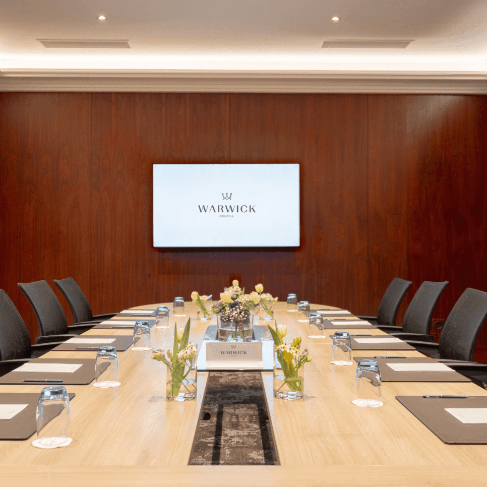 Long oval table by black mesh chairs under a wall-mounted screen in Gobelin at Warwick Geneva