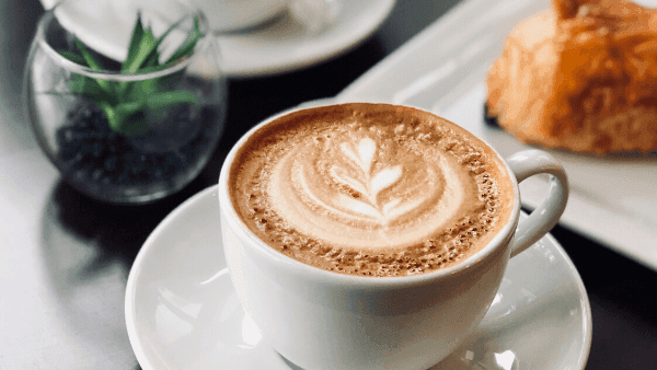 Beautifully crafted latte with leaf design next to a pastry served in the Deli Café & Market at Novotel Sunshine Coast Resort