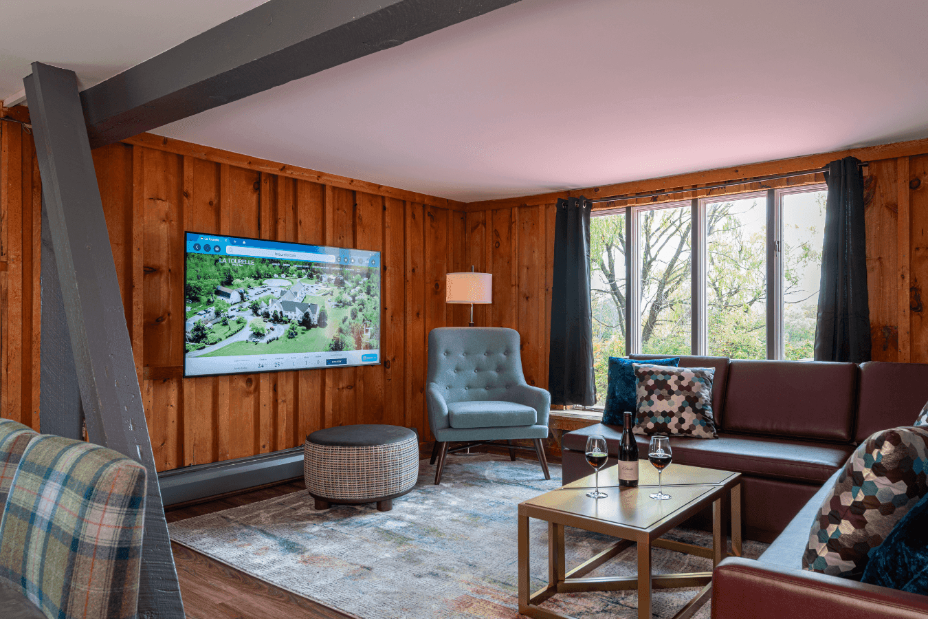 Wood-paneled lounge with a leather sectional and blue armchair by a wall-mounted TV and coffee table at La Tourelle Inn