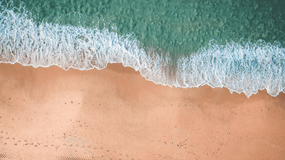 Aerial view of blue ocean waves meeting a clean sandy beach near Novotel Sydney International Airport