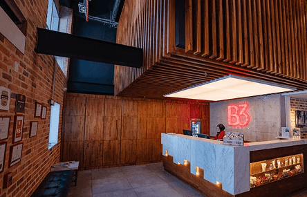 White marble reception desk lit by candles under a wood-slat ceiling, by a glowing red neon B3 sign at B3 Virrey Hotel