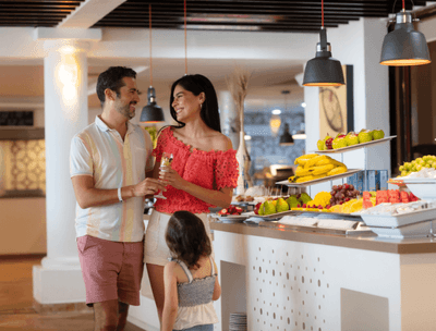 Family at a buffet with fruit and a variety of dishes on display in Frutas y Flores Restaurant at Buenaventura Grand Hotel and Spa