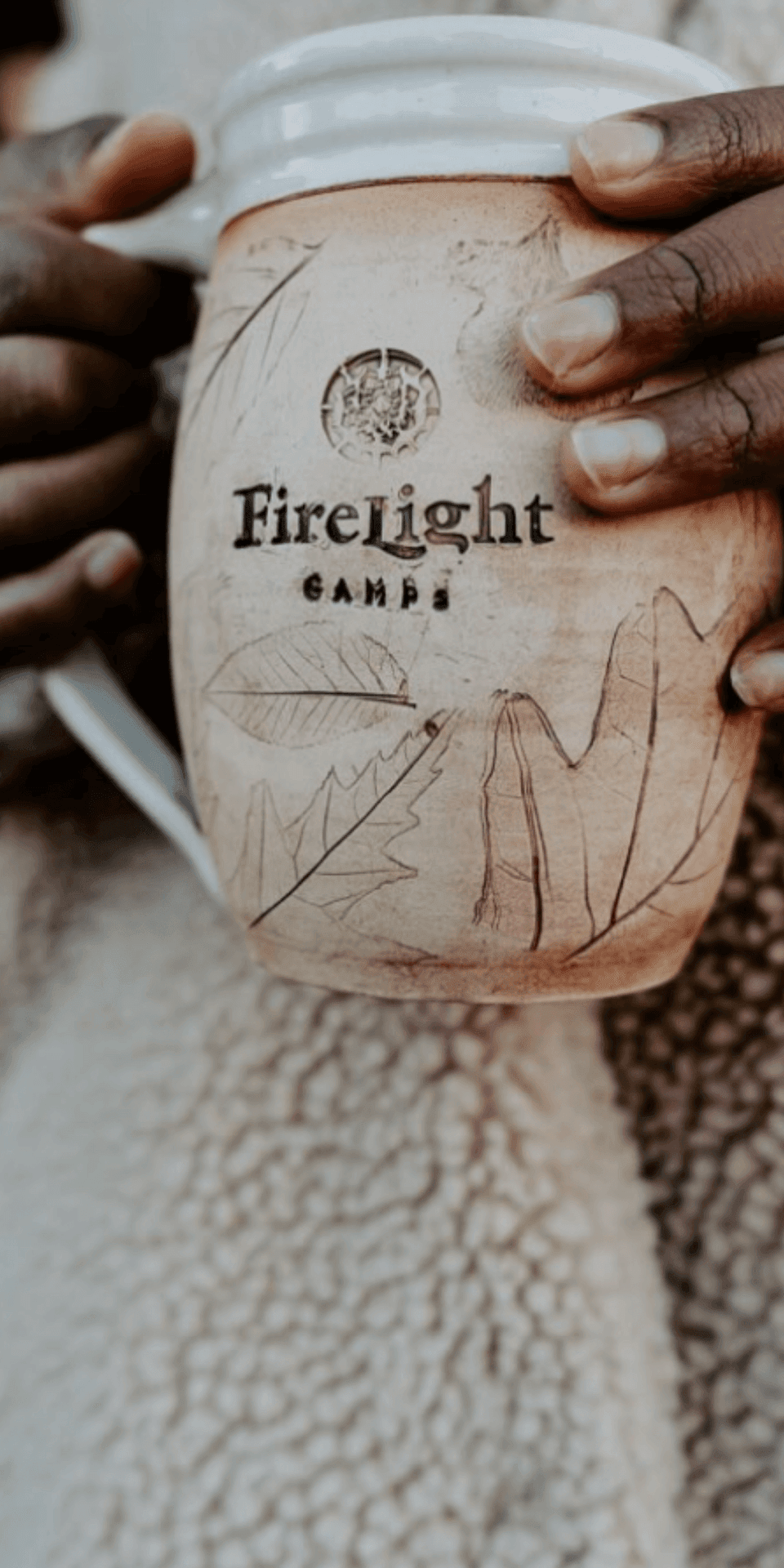 Close-up view of a ceramic mug with Firelight Camps leaf artwork held by hand at La Tourelle Hotel and Spa