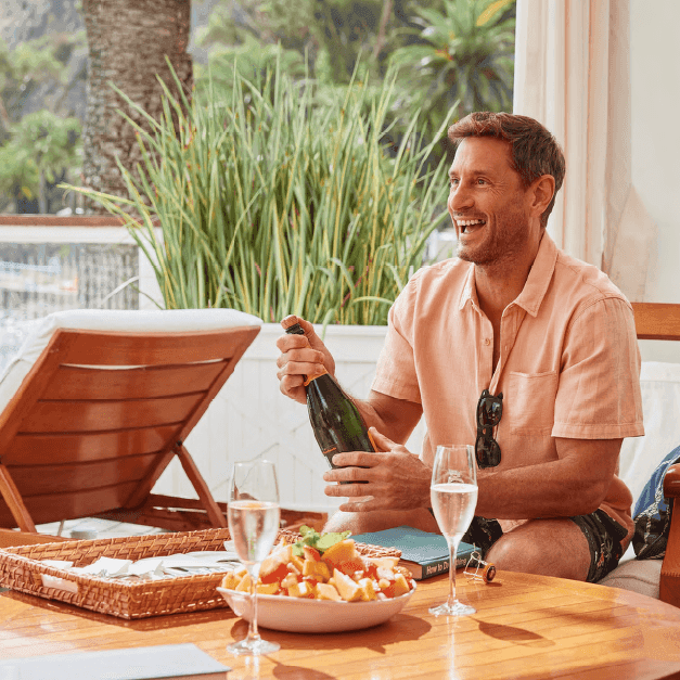 Man opening a champagne bottle while smiling at Catalina Island Company