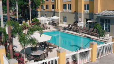 Sunny pool area with lounge chairs and tables under umbrellas by the fence at Galleria Palms Hotel