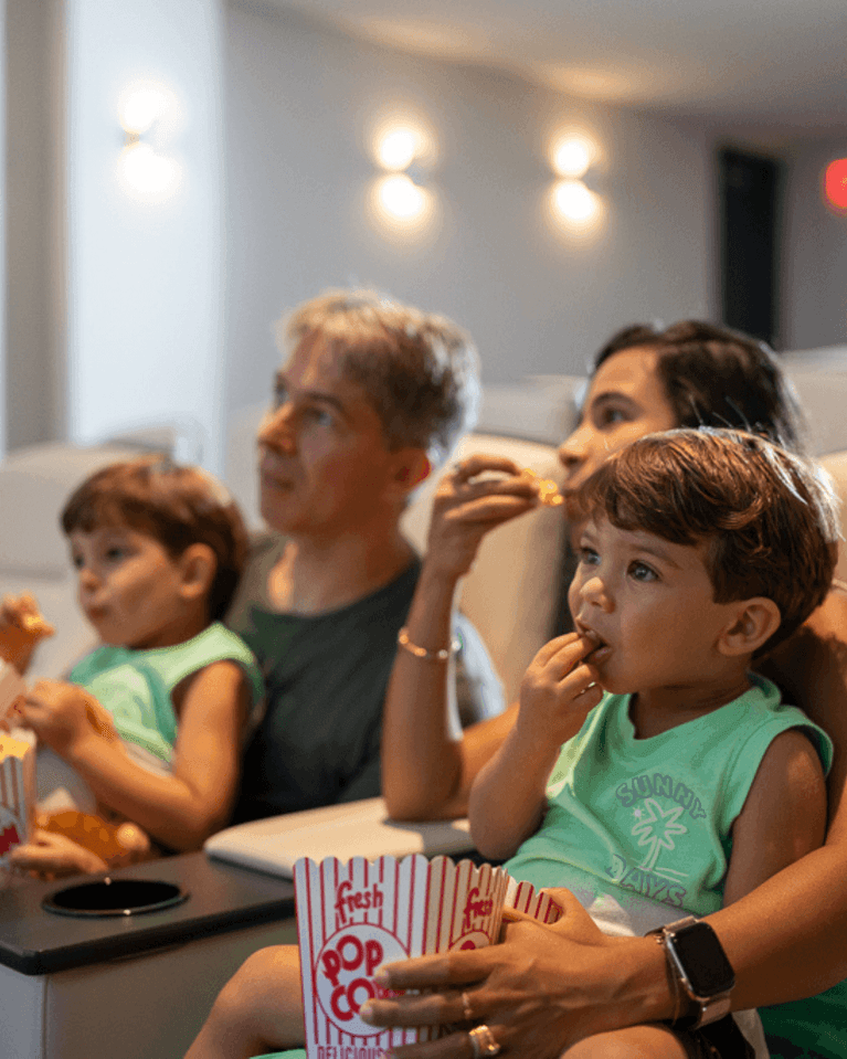 Family eating popcorn in plush theater seats under dim wall sconces in screening room at the Hotel X Toronto
