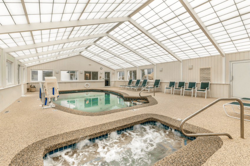 An indoor pool area with a pool, hot tub, lounge chairs, and a skylight.