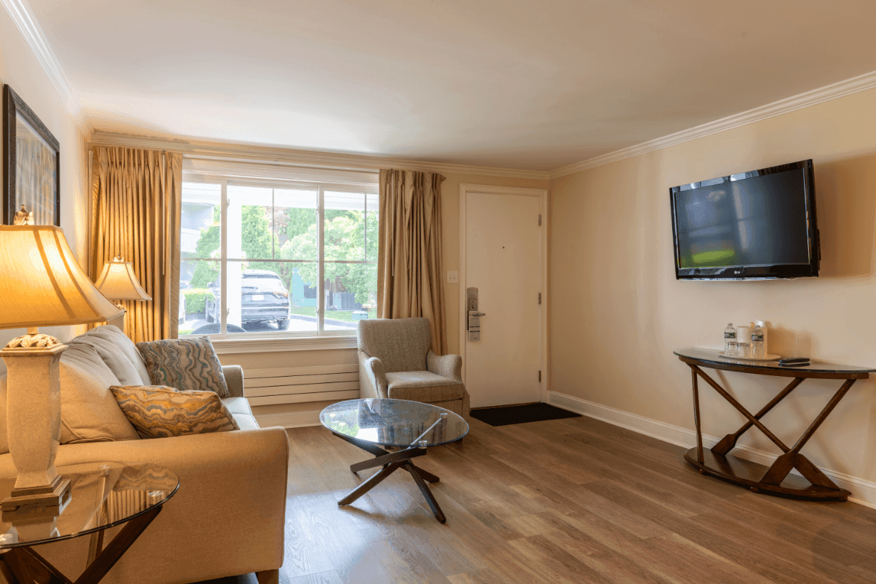 A hotel room with a sofa, armchair, coffee table, and TV on the wall.