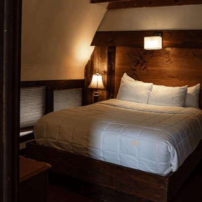 Cozy bed with white bedding under exposed wooden beams and warm wall lighting inside La Tourelle Hotel and Spa