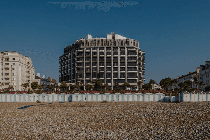 Exterior shot of The View Hotel building with balconies overlooking a pebble beach with blue and white beach huts