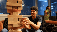 Young man playing giant Jenga in a modern communal lounge with blue walls and large windows at UniLodge
