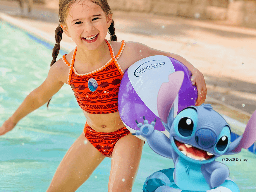 Young girl smiling in orange swimsuit holding inflatable character toy in sunny pool with Main Character Energy