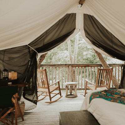 Glamping tent interior facing wooden deck balcony with rocking chairs and forest view at La Tourelle Hotel and Spa