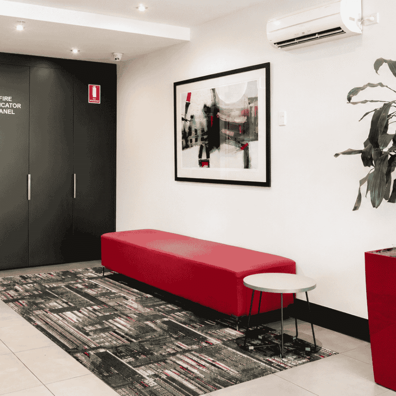 Modern lobby with red bench, abstract artwork, and potted plant at Student Living - Waymouth