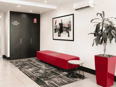 Modern lobby with red bench, abstract artwork, and potted plant at Student Living - Waymouth