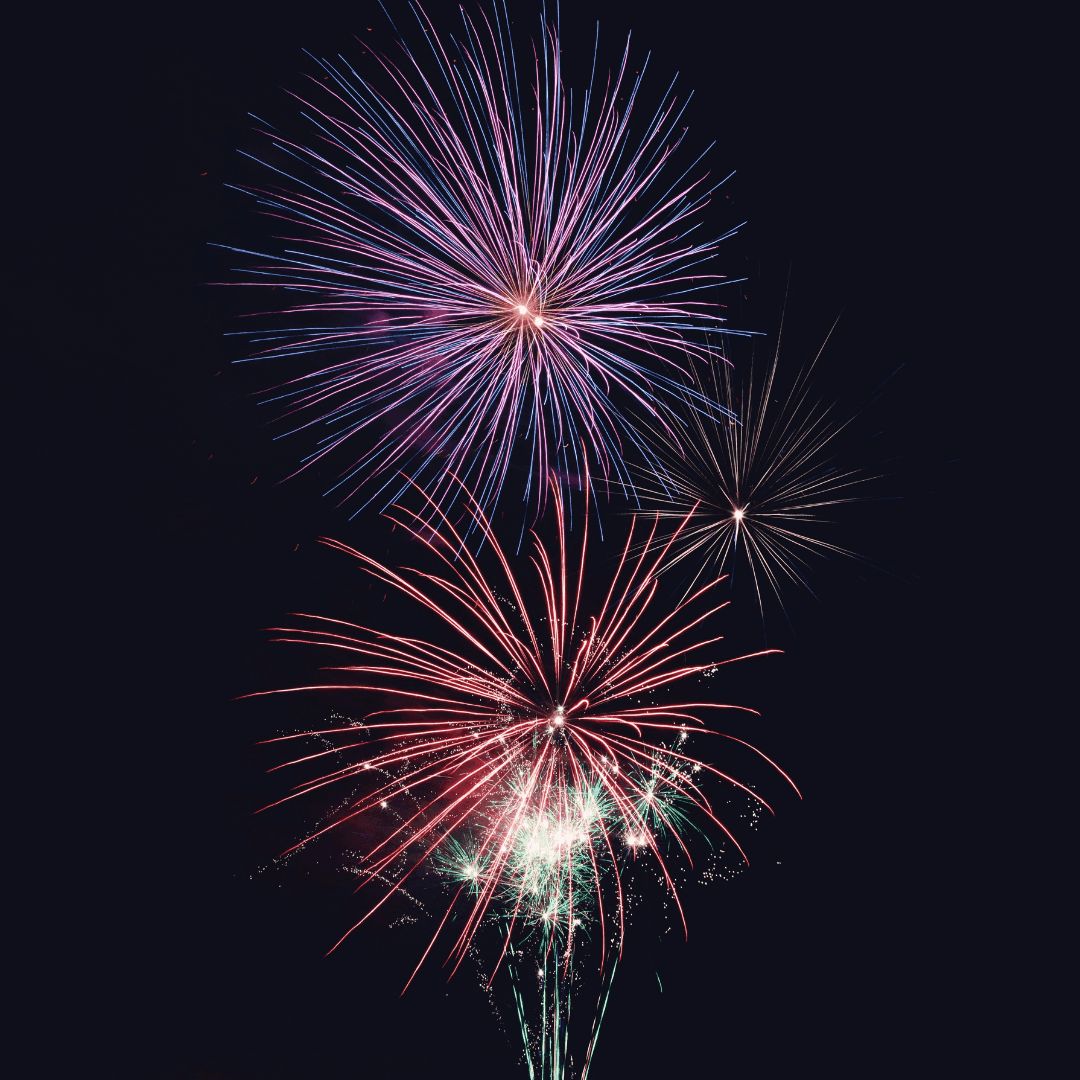 Three fireworks with red, green, and purple sparks burst against a dark night sky.