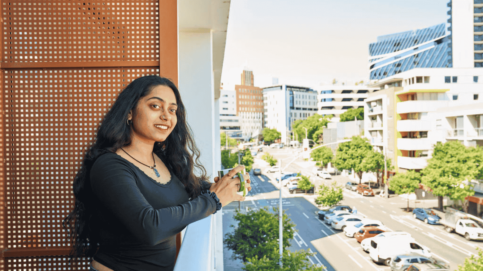 Woman on balcony at UniLodge Royal Melbourne overlooking street with cars and buildings.