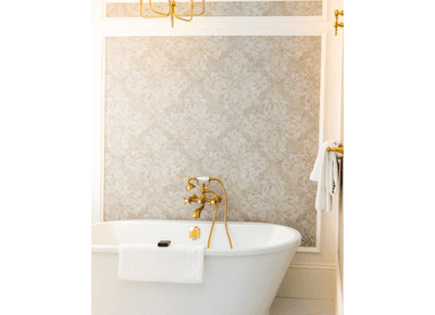 White freestanding bathtub featuring classic gold fixtures against a patterned wallpaper wall at Rodd Hotels & Resorts